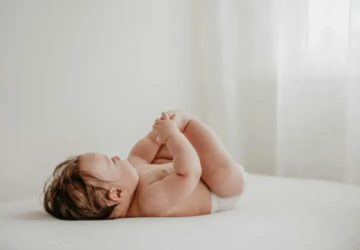 Un neonato con un adorabile culetto rosso, sdraiato su un lettino, gioca con i suoi piedini.