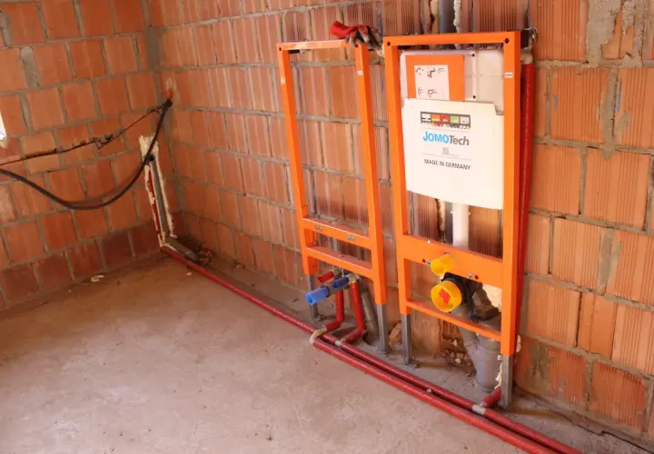 Instalacja hydrauliczna przed tynkami: stelaże podtynkowe, rury i spłuczka JomoTech w budowie.