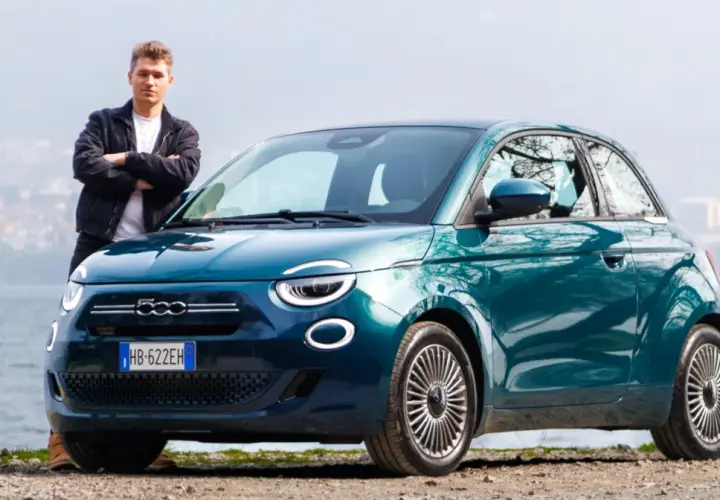Młody mężczyzna stoi obok swojego nowego, turkusowego fiat mini 500 nad jeziorem.