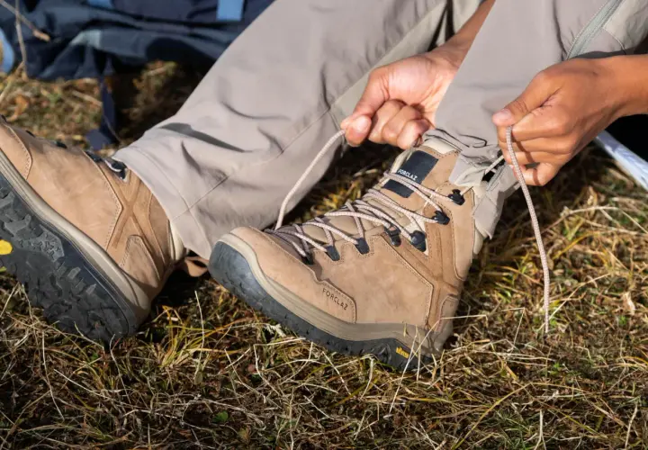 Ręce zaciskają sznurówki brązowego buta trekkingowego. Solidna podeszwa buta zapewnia przyczepność na nierównym terenie.