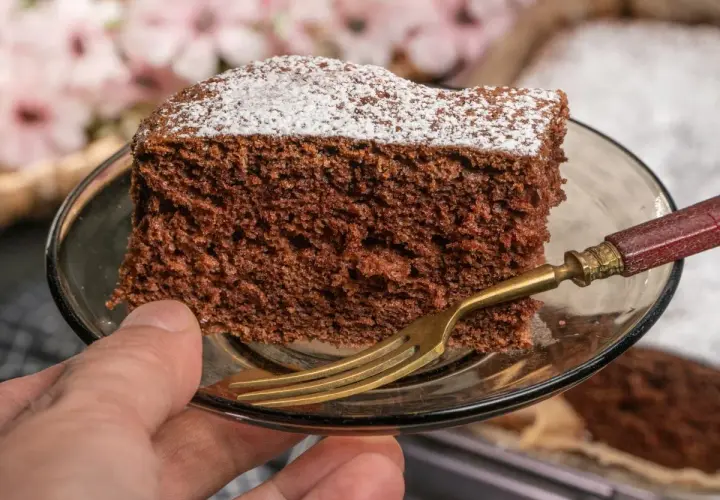 Kawałek najprostszego ciasta czekoladowego, posypana cukrem pudrem, na talerzyku z widelcem.