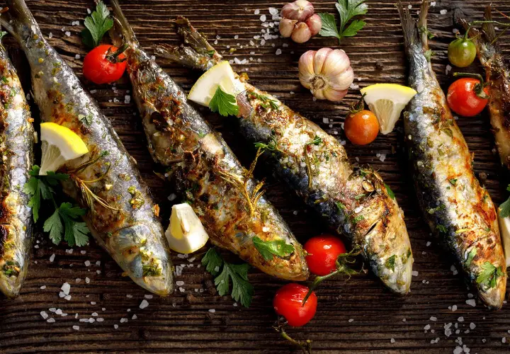 Sardines grillées, citron, tomates cerises et ail sur fond de bois. Faut-il vider les sardines avant de les cuire ?