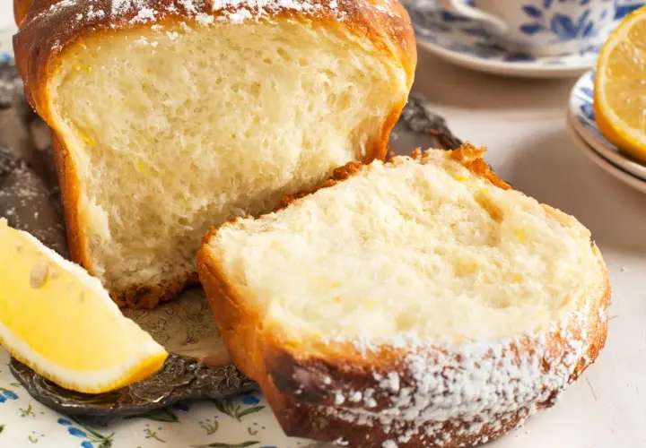 Puszyste ciasto drożdżowe bez mleka, posypane cukrem pudrem, z plasterkiem cytryny obok. Idealne na śniadanie.