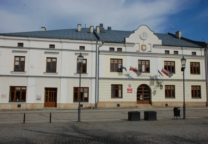 Rektorat w mieście, gdzie kierunkowy 13 wskazuje drogę. Budynek z zegarem i polskimi flagami.