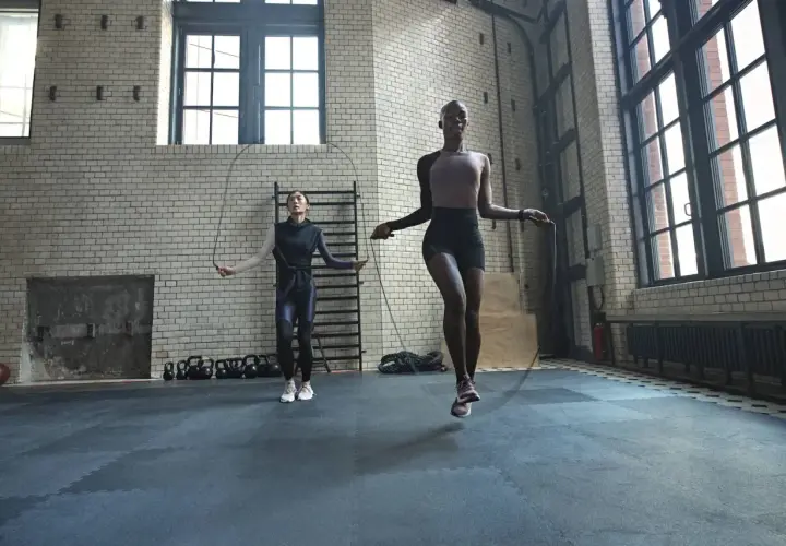 Dos mujeres realizan un calentamiento antes de hacer ejercicio, saltando la cuerda en un gimnasio industrial.