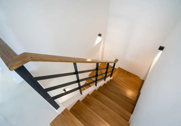 Nowoczesne oświetlenie klatki schodowej w domu jednorodzinnym, z drewnianymi stopniami i czarną balustradą.