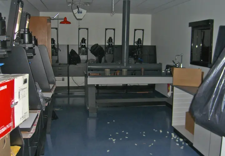 Wnętrze ciemni fotograficznej z kilkoma powiększalnikami, stołem laboratoryjnym i zlewem.