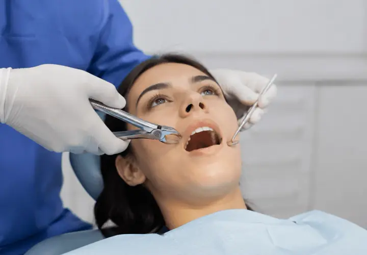 Dentista usa fórceps para sacar muelas a paciente con boca abierta.
