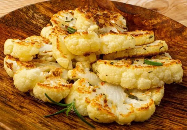 Tranches de chou-fleur rôti, dorées et garnies d'herbes, servies sur un plat en bois.