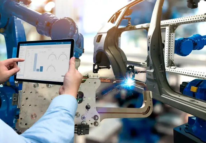 Ein Roboter schweißt ein Autoteil, während ein Mensch auf einem Tablet die Produktionsdaten prüft. Was ist eine BOM? Hier wird sie digital verwaltet.