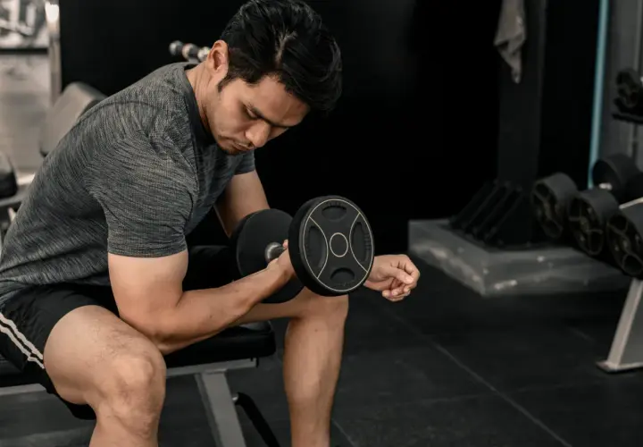 Mężczyzna ćwiczy biceps z hantlem. Energia do treningu pochodzi z glikogenu, który jest zapasem cukru w mięśniach.