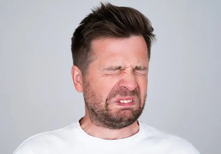Mężczyzna z wykrzywioną twarzą, oczy zamknięte, czuje gorzki smak w ustach.