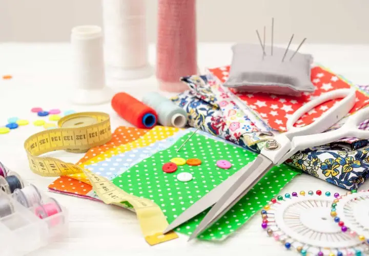 A collection of 10 sewing tools: scissors, measuring tape, spools of thread, needles, buttons, and fabric scraps, ready for a creative project.