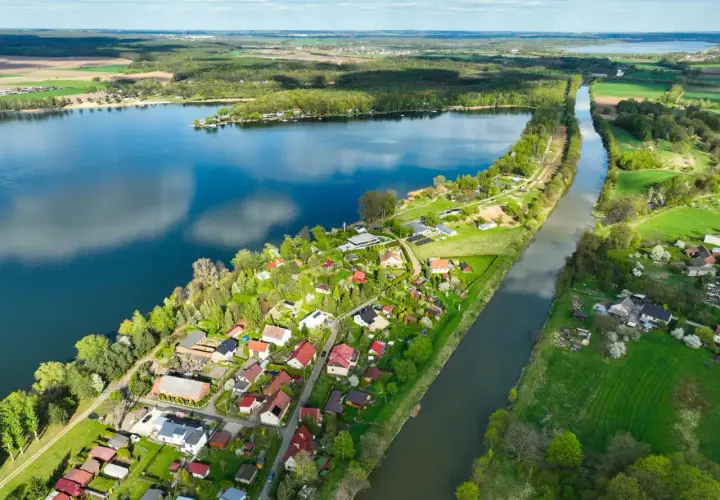 Malownicze jezioro Pławniowice z kanałem i zabudowaniami w otoczeniu zieleni.