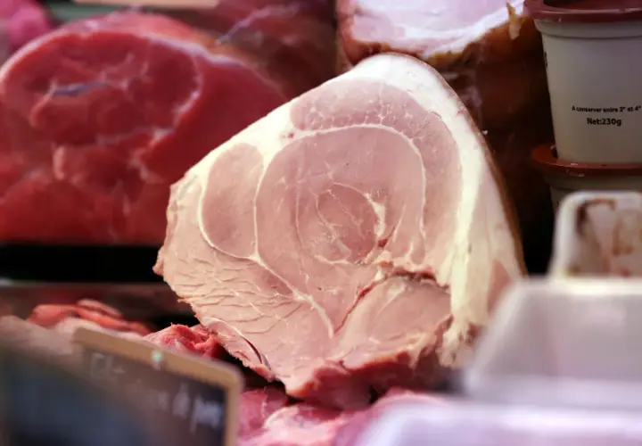 Gros plan sur une pièce de viande rose pâle, probablement une côte de porc, avec des marbrures de gras. Derrière, on aperçoit de la viande rouge vif.