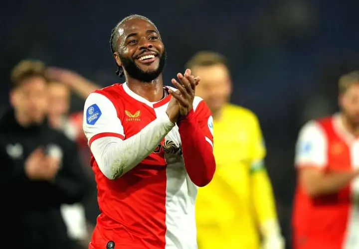 Uśmiechnięty Raheem Sterling w czerwono-białej koszulce, klaszczący. Jego statystyki w tym sezonie są imponujące.