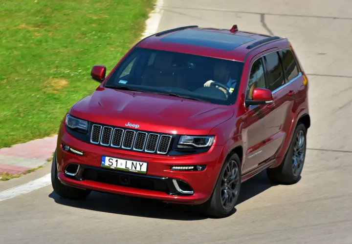 Czerwony Jeep Grand Cherokee z kierowcą za kierownicą, indywidualni na drodze, pokonuje zakręt na torze wyścigowym.