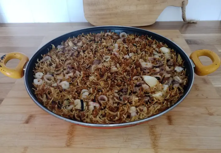 Fideos fideuá con calamares y gambas, listos para servir en una paellera.