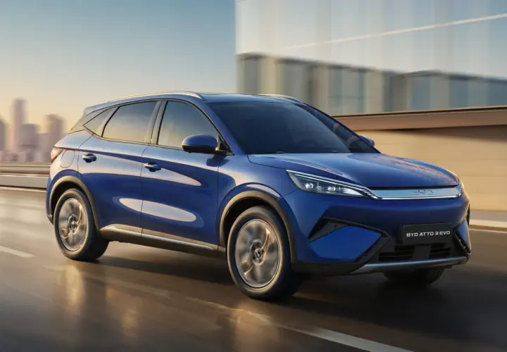 BYD Atto 3 blu in movimento, con la sua notevole autonomia, sfreccia su una strada urbana al tramonto.