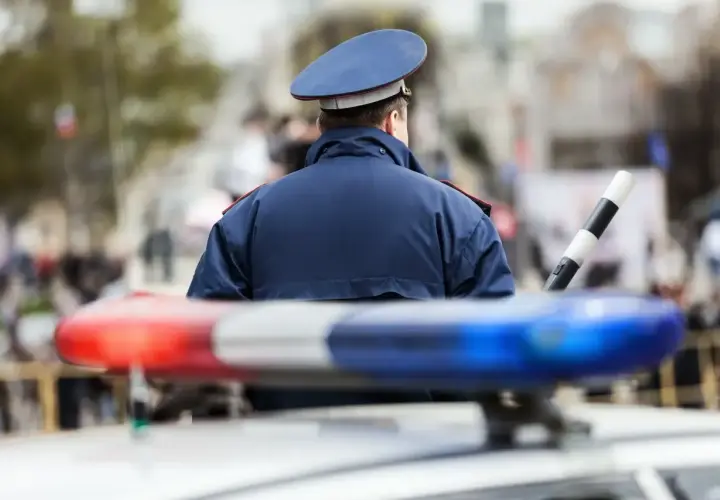 Policjant w mundurze stoi przy radiowozie. Zastanawiasz się, ile zarabia policja kryminalna?