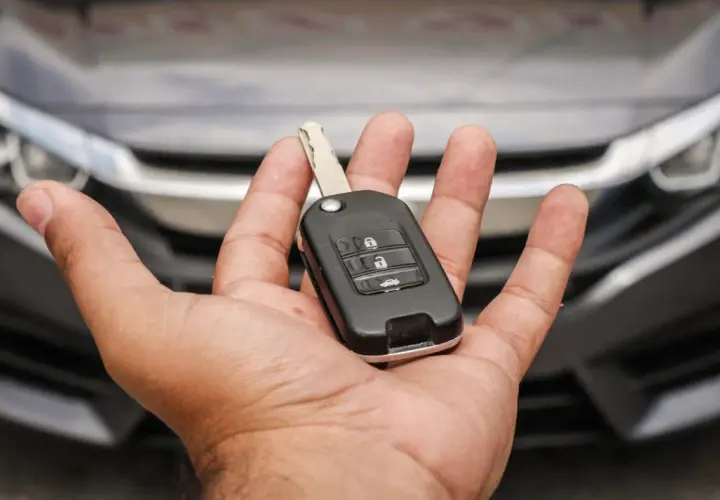 Mano che tiene una chiave auto moderna, pronta per duplicare la chiave auto. Auto scura sullo sfondo.