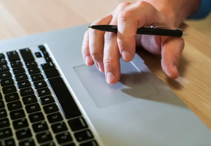 Mano con bolígrafo sobre el touchpad de un portátil, como si buscara qué es un hash.