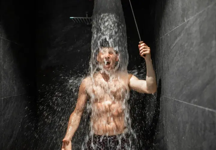 Mężczyzna krzyczy, gdy zimny prysznic wieczorem obmywa jego ciało. Woda spływa po jego klatce piersiowej, tworząc kaskadę.
