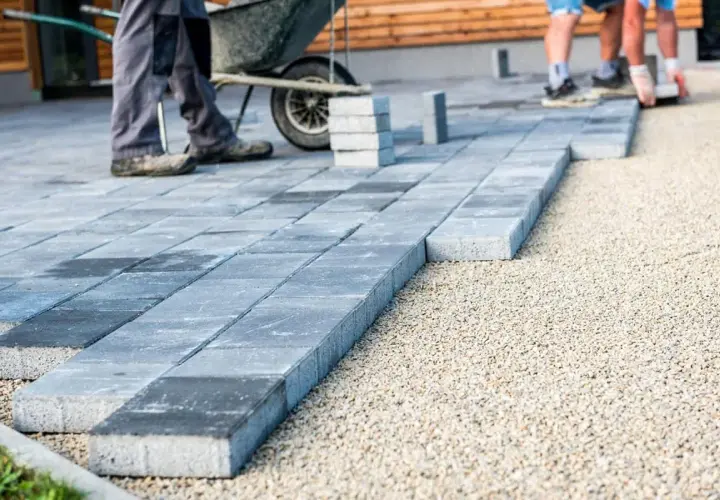 Układanie betonowych płyt na żwirze. Pracownicy tworzą nowoczesny taras, gdzie beton zamiast kostki nadaje mu minimalistyczny charakter.