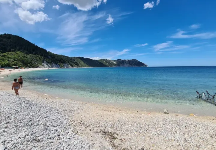 Spiaggia di Portonovo con il Monte Conero sullo sfondo. Acqua cristallina e cielo azzurro.