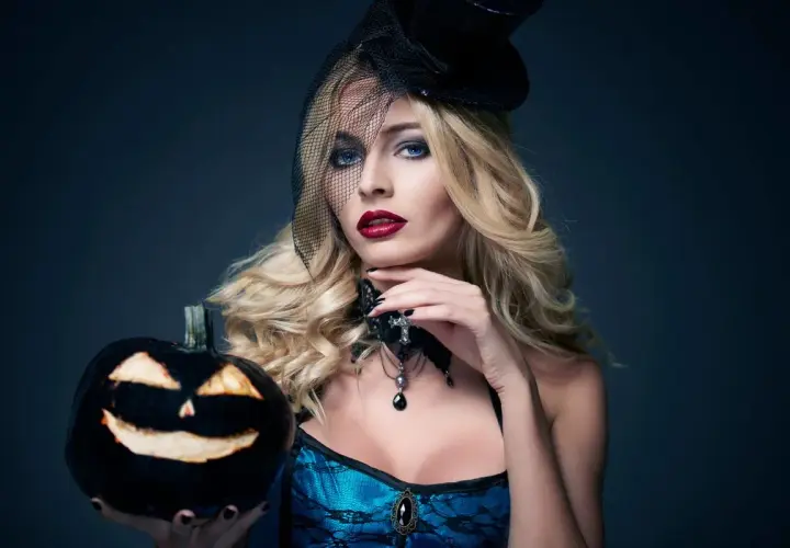 Kobieta z blond włosami i makijażem na Halloween trzyma wydrążoną dynię. Jej fryzury na Halloween są idealne na imprezę.