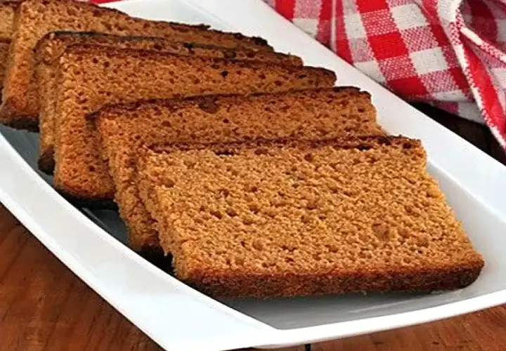 Tranches de pain d'épices moelleux disposées sur un plat blanc, avec un torchon à carreaux rouges en arrière-plan.
