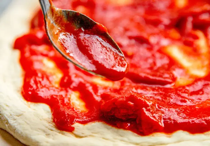 Cuchara esparciendo deliciosa salsa para pizza sobre la masa.