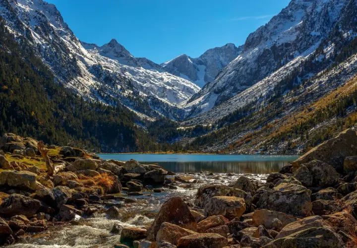 Majestuosas montañas nevadas flanquean el sereno lac de Gaube, con un arroyo rocoso que desemboca en sus aguas turquesas.