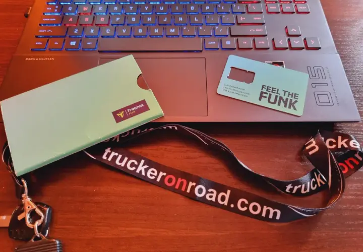 Karta SIM "Feel the Funk" i klucze na smyczy "truckeronroad.com" leżą obok laptopa. Czas na pauzę 45h bez karty w tachografie.