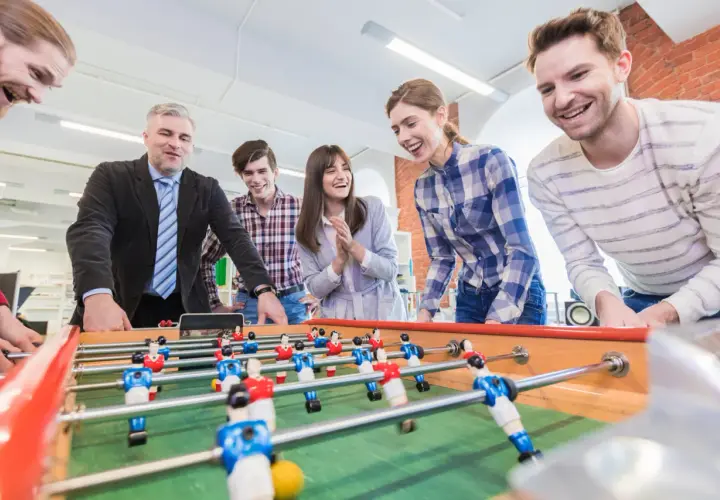 Colleagues laugh and play foosball, showcasing great employee engagement games.