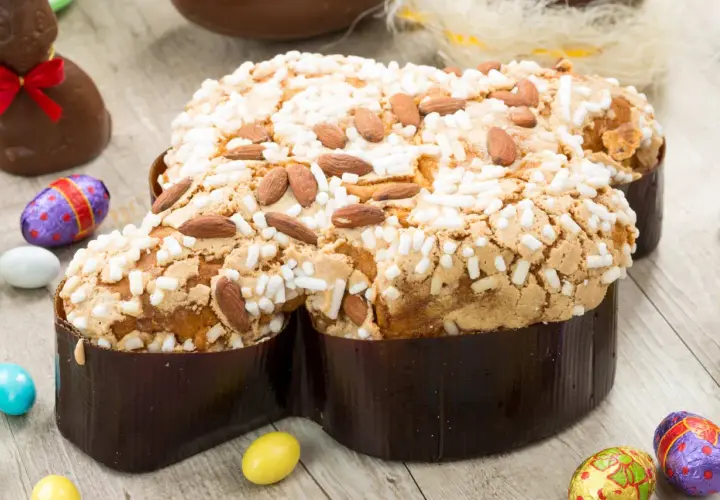 Colomba pasquale ricetta: dolce soffice con mandorle e glassa croccante, circondata da uova di cioccolato e coniglietti.