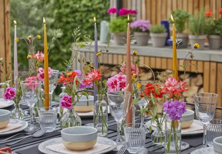 Tavola apparecchiata con candele colorate e fiori freschi, un'ispirazione per decorazioni estive fai da te.