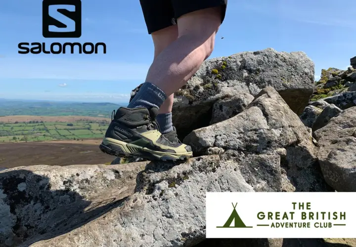 Stopy w butach Salomon X Ultra 5 Mid GTX na skalistym szlaku, z widokiem na zielone wzgórza.
