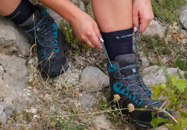 Hands tying the laces of a dark grey hiking boot with teal accents. Learn how to wear hiking boots for your next adventure.