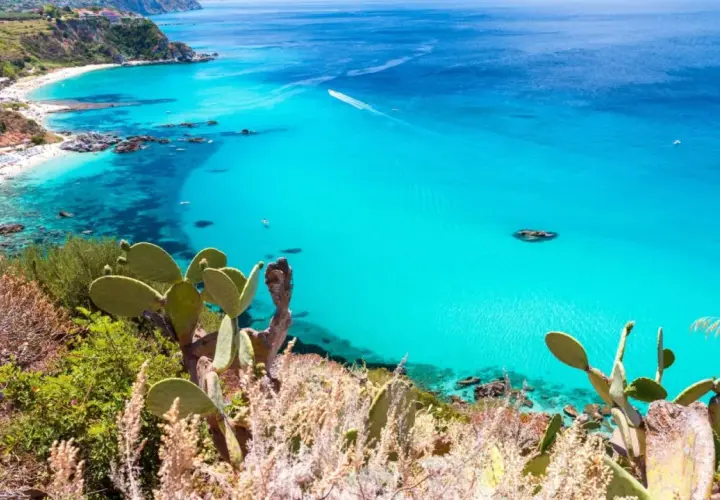 A stunning view of Reggio Calabria beaches, with turquoise waters, white sand, and lush green cliffs dotted with cacti.