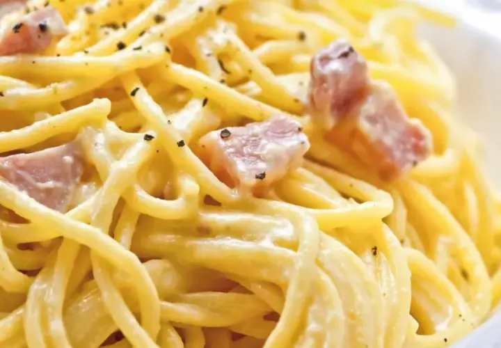 Ein Teller Spaghetti Carbonara, klassisch italienisch zubereitet mit cremiger Sauce und Speckwürfeln, bestreut mit schwarzem Pfeffer.