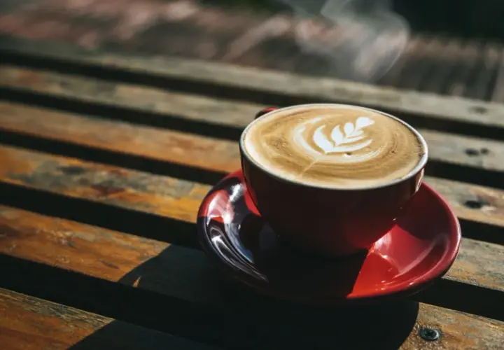 Czerwona filiżanka kawy latte z wzorem na piance, parująca na drewnianym stole. Czy kawę Inkę można pić wieczorem?