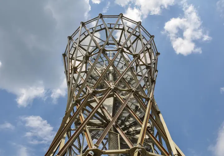 Metalowa konstrukcja wieży widokowej, przypominająca spiralę, wznosi się ku niebu. W oddali widać borowa góra.
