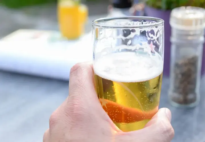 Chłodne piwo Miller w szklance, z bąbelkami i pianką, w letnim ogródku.