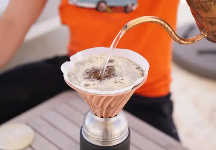 Heißes Wasser fließt aus einer Kupferkanne in einen Filter, um köstlichen Kaffee zu machen.