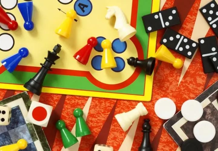 Bunte Spielfiguren, Würfel, Dominosteine und Schachfiguren liegen verstreut. Eine bunte Mischung bekannter Brettspiele für endlosen Spielspaß.
