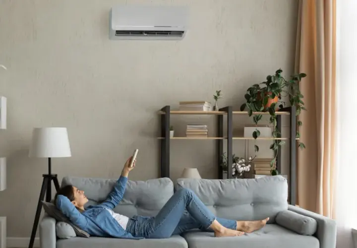 Mujer relajada en el sofá, usando el control remoto para programar el aire acondicionado y disfrutar de la temperatura perfecta.