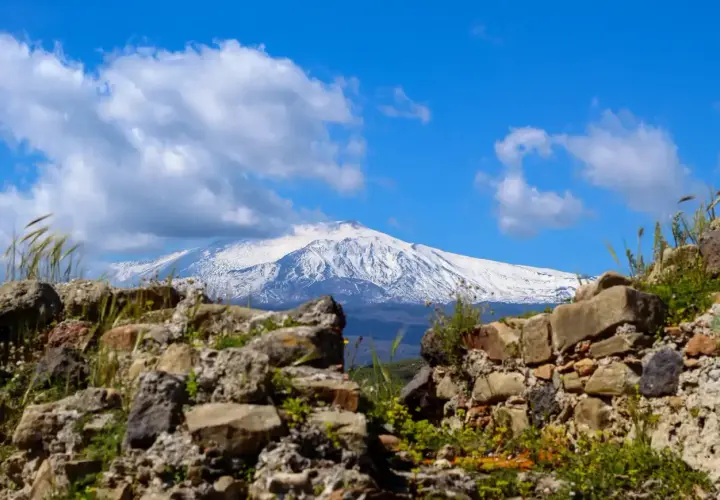 Rovine antiche incorniciano la maestosa vista dell'Etna innevato, un paesaggio iconico di Taormina.