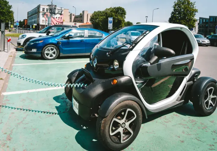 Mały, elektryczny pojazd, którym można jeździć bez prawa jazdy, ładuje się obok innych samochodów elektrycznych.