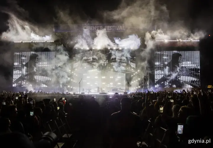 Koncert Linkin Park Polska na Open'er Festival. Tłum ludzi z telefonami, dym i światła na scenie.